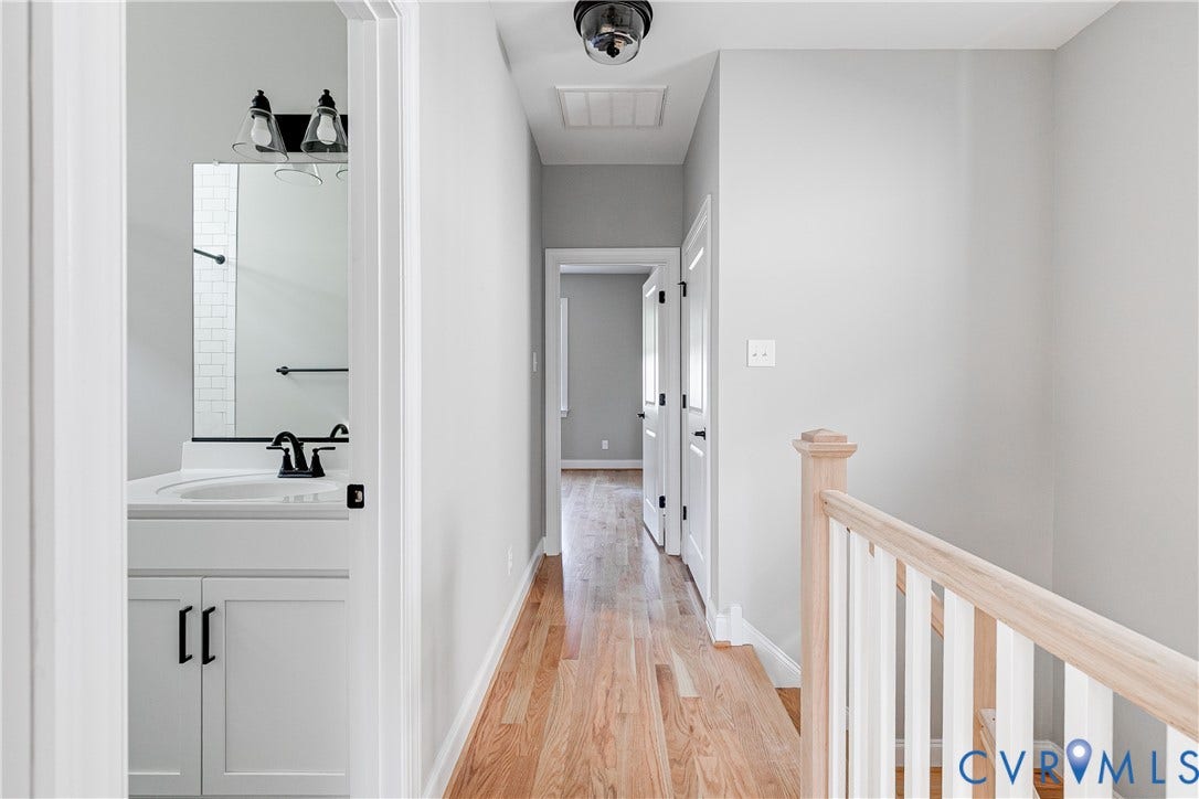 Hardwood flooring throughout, white painted walls, white spindle railing, white vanity with black hardware, and a black faucet
