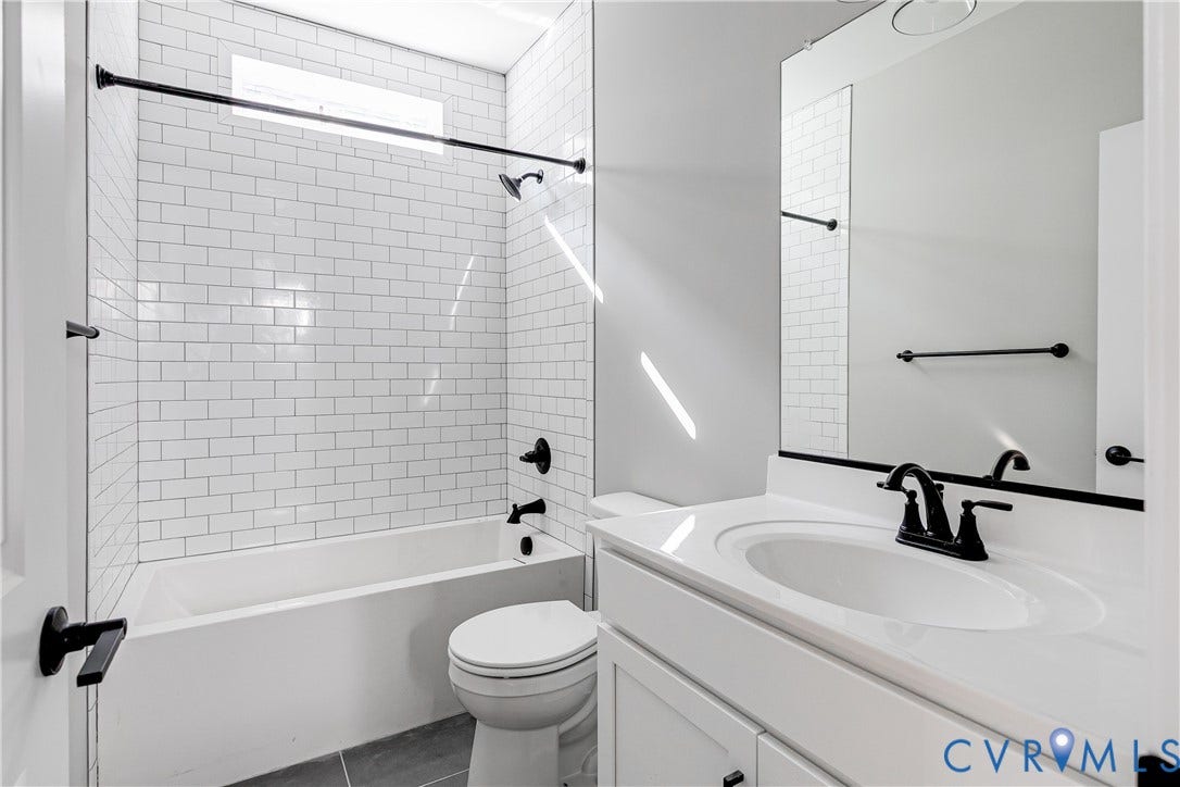 Tub and shower combination with white subway tile surround, white vanity with integrated sink, black fixtures, and a large wall-mounted mirror