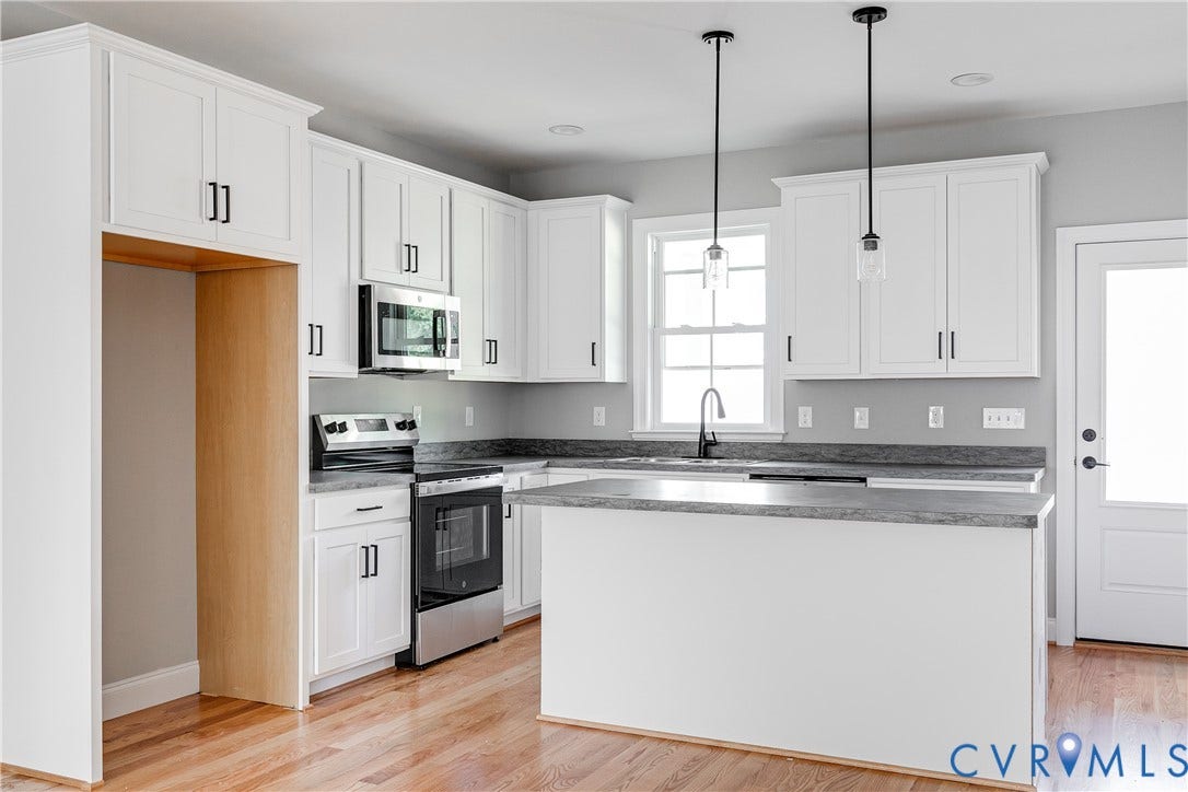 White shaker cabinetry, stainless steel appliances, central island with countertop, wood-finish flooring, and pendant lighting
