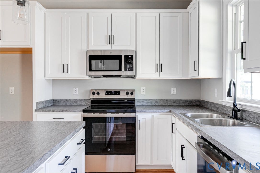 Kitchen featuring white shaker cabinetry, stainless steel appliances, dark countertops, a double basin sink, and a gooseneck faucet
