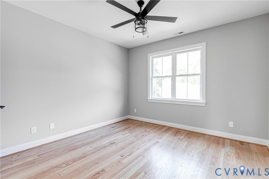 Hardwood-finish flooring, light gray wall finishes, white trim, a double-hung window, and a ceiling fan with integrated lighting
