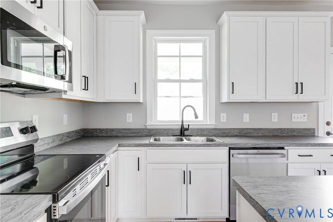 Kitchen featuring white cabinetry, stainless steel appliances, a double basin sink with a black faucet, and patterned countertops