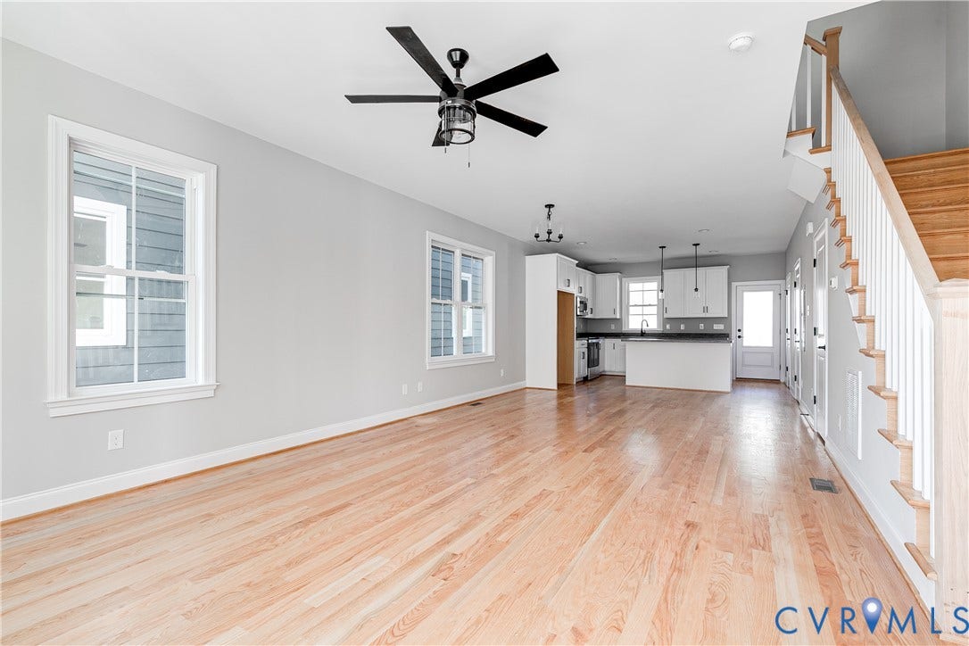 Open-concept floor plan featuring wood-finish flooring, white cabinetry, dark countertops, and a staircase with white risers and wood treads