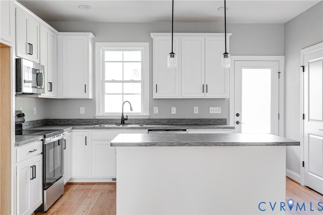 Kitchen featuring white cabinetry, stainless steel appliances, dark countertops, a central island, and wood-finish flooring