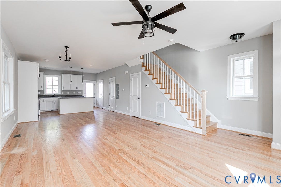 Light wood-finish flooring, white painted walls, white kitchen cabinetry, a kitchen island, and a dark-toned ceiling fan