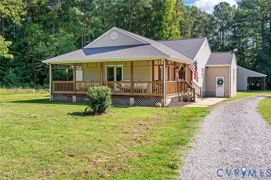 Expansive front yard with a gravel driveway, covered front porch, and an attached storage shed