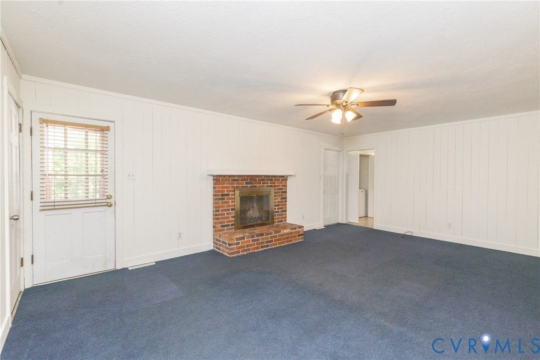 2765 Briarpatch Lane, Powhatan, VA 23139 Spacious living area featuring blue carpet flooring, white vertical shiplap walls, and a brick fireplace with dark surround