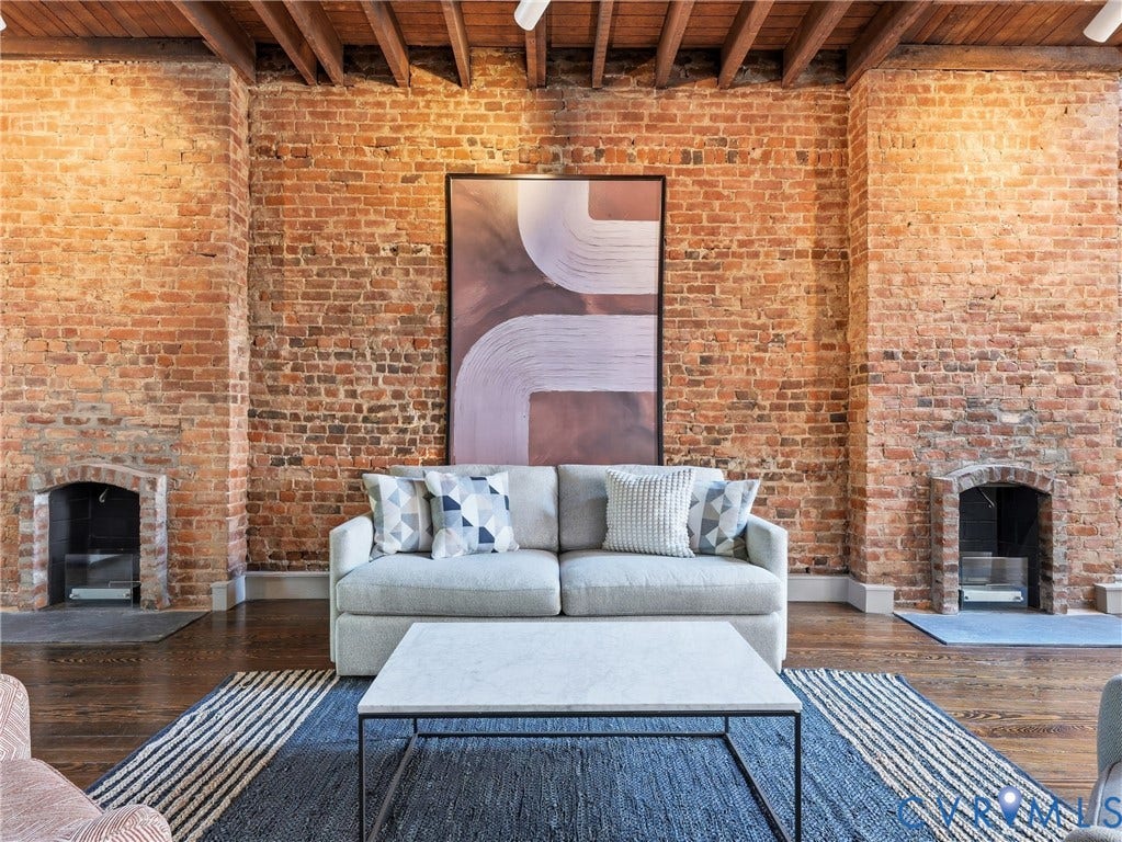 Exposed brick walls, two brick fireplaces, wood-finish flooring, and an exposed beam ceiling