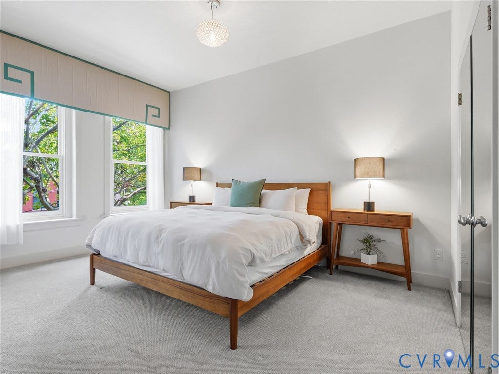 Bright interior with two double-hung windows, a decorative valance, a crystal chandelier, and light-colored carpeting