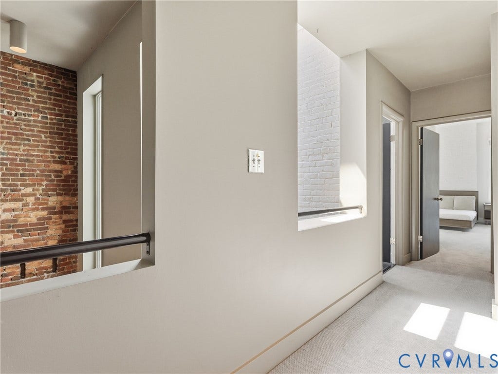 Hallway with light-toned wall finishes, light-toned carpeting, and a built-in railing