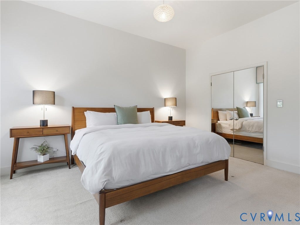 White wall paint, light-colored carpeting, spherical ceiling light fixture, wood-finish bed frame, mirrored closet doors