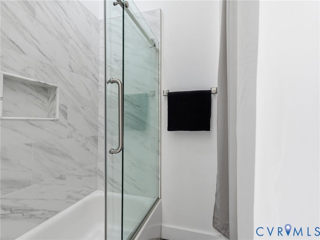 Bathtub with a glass sliding shower door, integrated storage niche, and marble-look tile surround