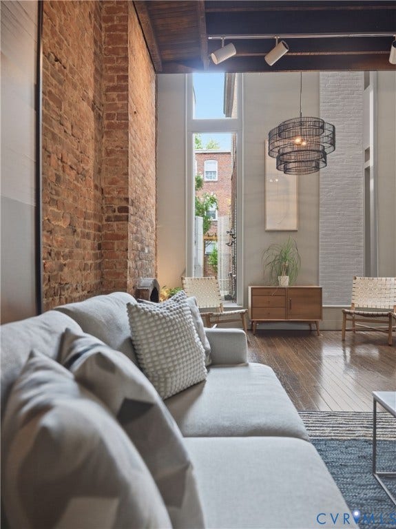 Exposed brick accent wall, wood-finish flooring, high ceilings with track lighting, and a tiered wire pendant light fixture