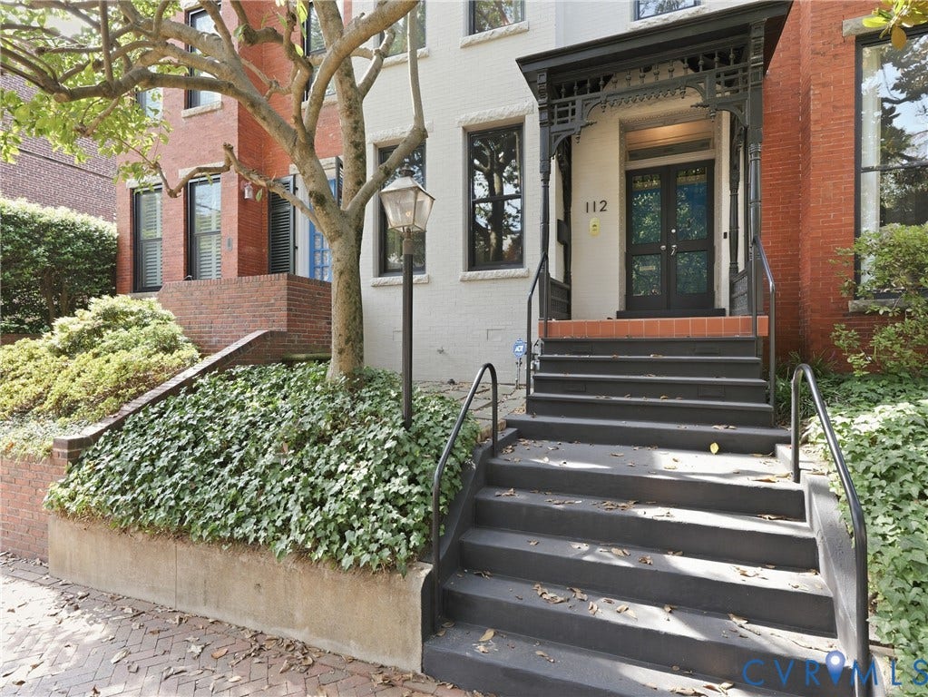 Entryway featuring ornate ironwork canopy, black double doors with glass panels, brick risers, and black railings