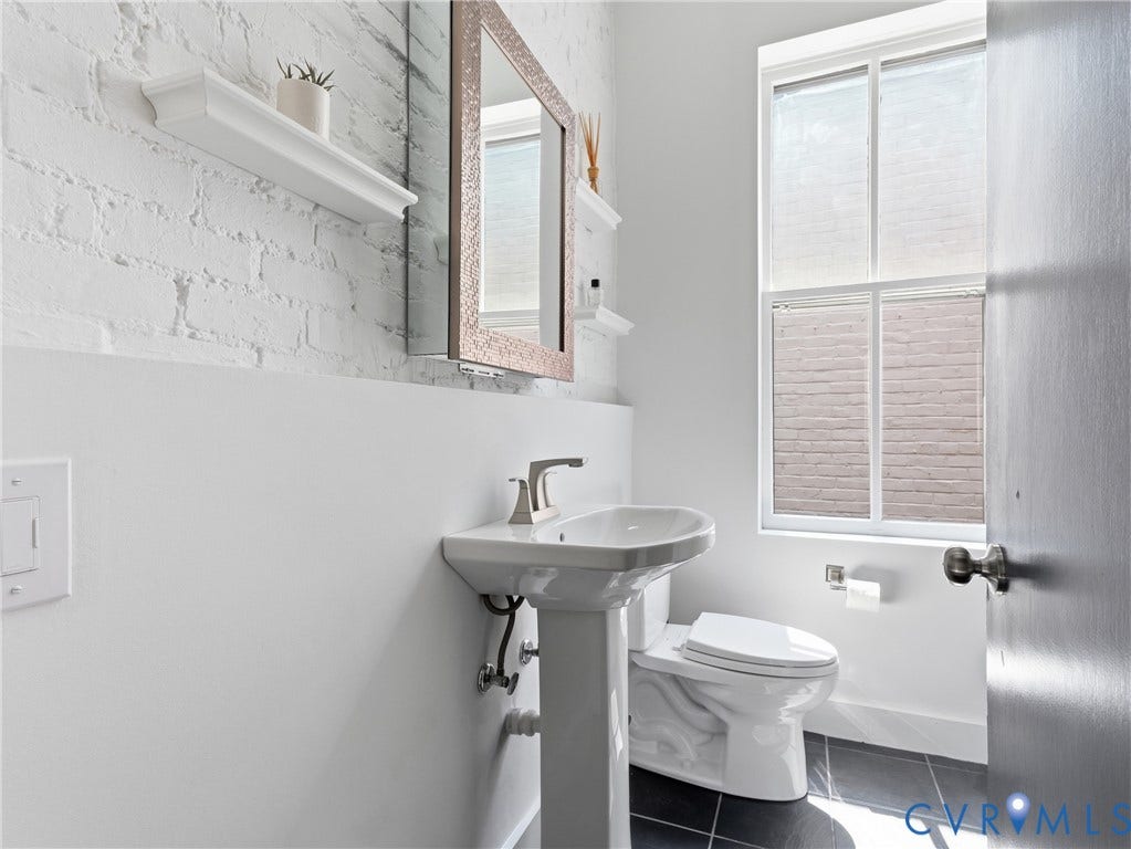 Pedestal sink with a brushed nickel faucet, framed mirror, and a white brick-finish wall