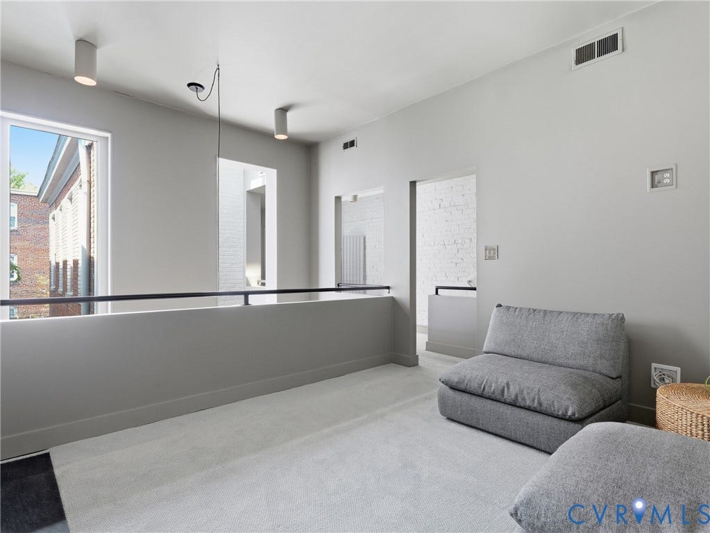 Carpeted loft space with a black metal railing, contemporary ceiling-mounted lighting, and a window