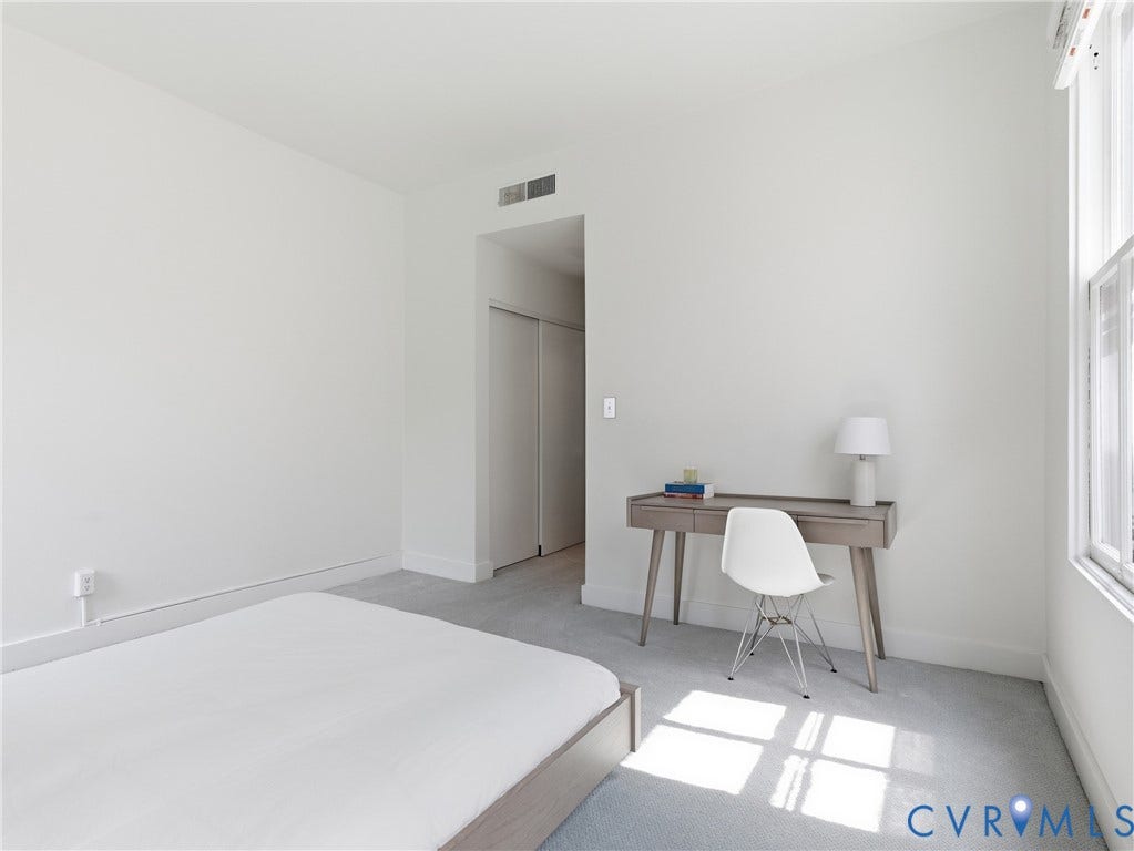 Light-toned carpeting, ample natural light from a window, and a built-in closet with sliding doors