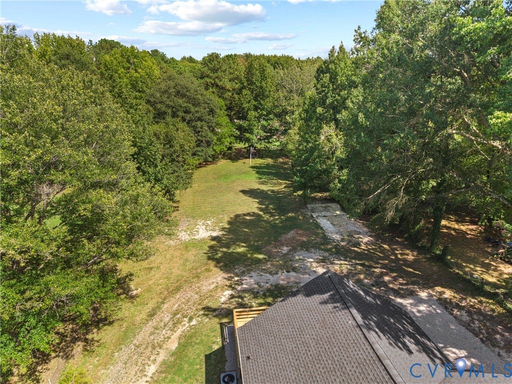 821 Fort Lee Road, North Dinwiddie, VA 23803 Expansive wooded lot with dense tree lines, a grassy clearing, and a partial view of the property's roofline
