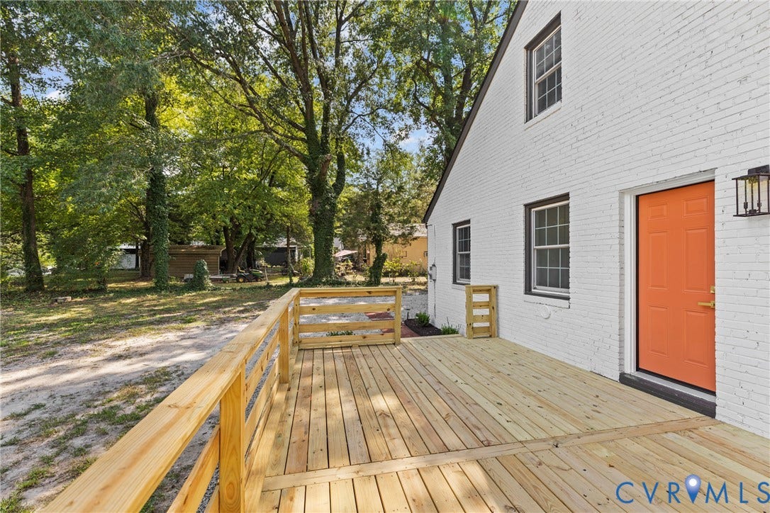 821 Fort Lee Road, North Dinwiddie, VA 23803 Expansive wood deck with a natural wood railing, white brick exterior, black window frames, and an orange entry door with a black exterior light fixture