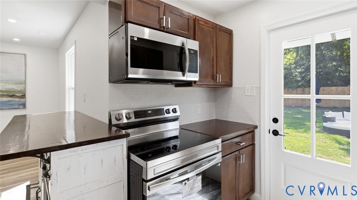 Stainless steel electric range, stainless steel microwave, dark wood-finish cabinetry, white tile backsplash, and a glass-paned exterior door