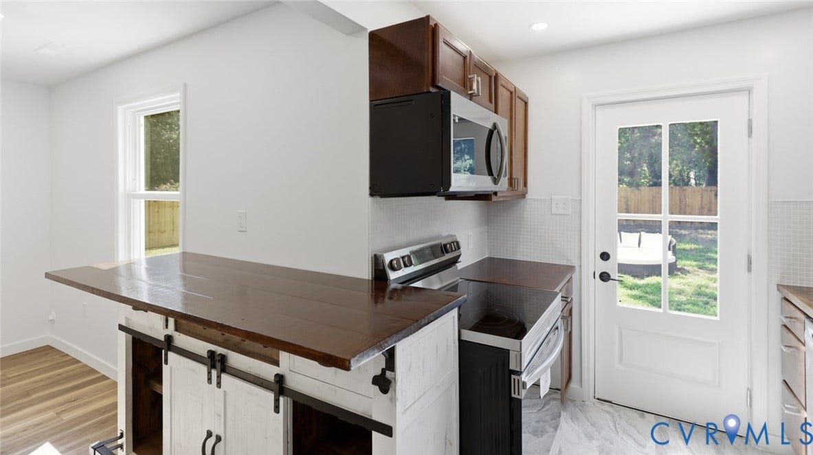 Kitchen featuring wood-finish cabinetry, stainless steel appliances, a tile backsplash, and a paneled exterior door