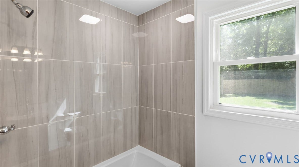 Tiled shower surround featuring a chrome showerhead and control, white bathtub, and a window with white trim
