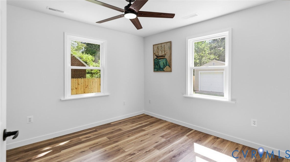 Wood-finish flooring, white walls, two double-hung windows, and a ceiling fan with light fixture