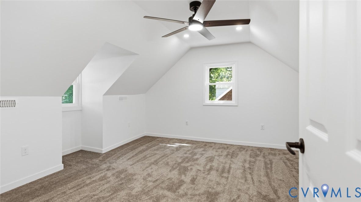 Vaulted ceiling room featuring a ceiling fan with integrated lighting, two windows, carpet flooring, and a white paneled door with dark hardware
