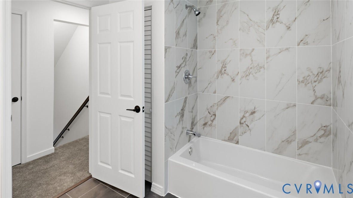 White bathtub with wall-mounted showerhead, surrounded by large format tiled walls