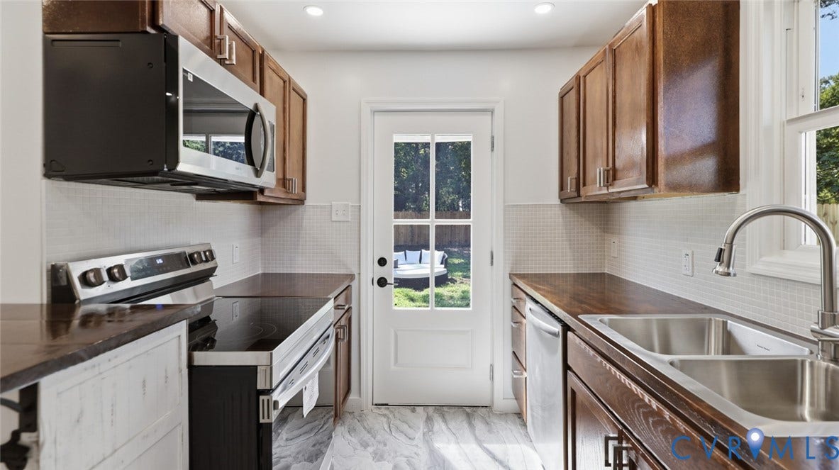 Wood-finish cabinetry, stainless steel appliances, wood-finish countertops, subway tile backsplash, and a double-basin sink