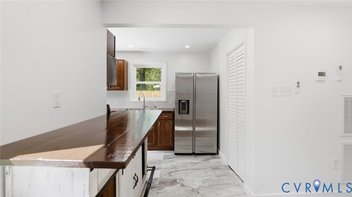 Wood-finish countertop with white base, stainless steel refrigerator, louvered bi-fold closet doors, and recessed lighting