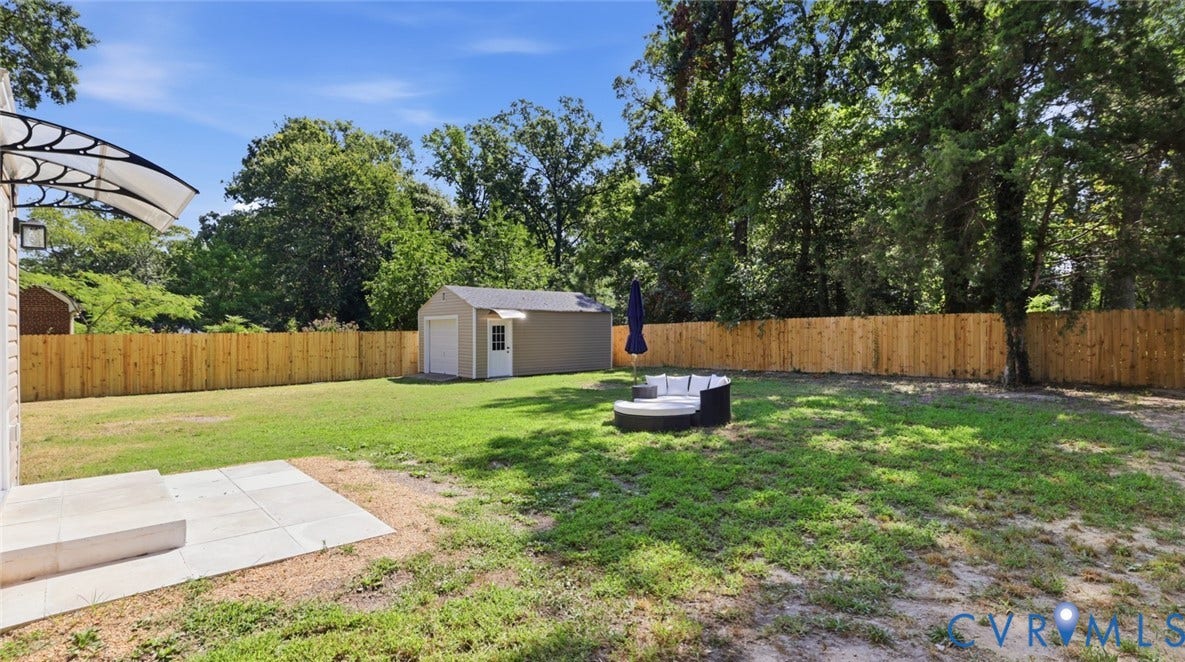 Expansive backyard featuring a new privacy fence, a detached shed, a paved patio, and mature trees