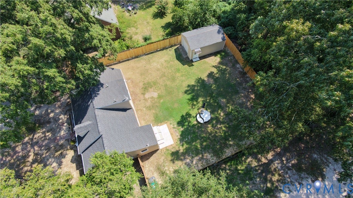 Expansive fenced backyard with a detached storage shed, lush green space, and mature perimeter trees