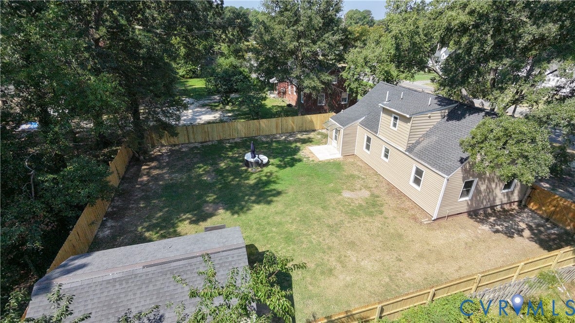 Expansive backyard featuring a manicured lawn, established trees, privacy fencing, and a concrete patio