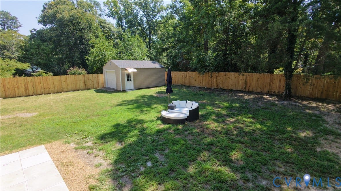 Expansive lawn area with a wood privacy fence, a detached shed with a roll-up door, and mature trees providing natural screening