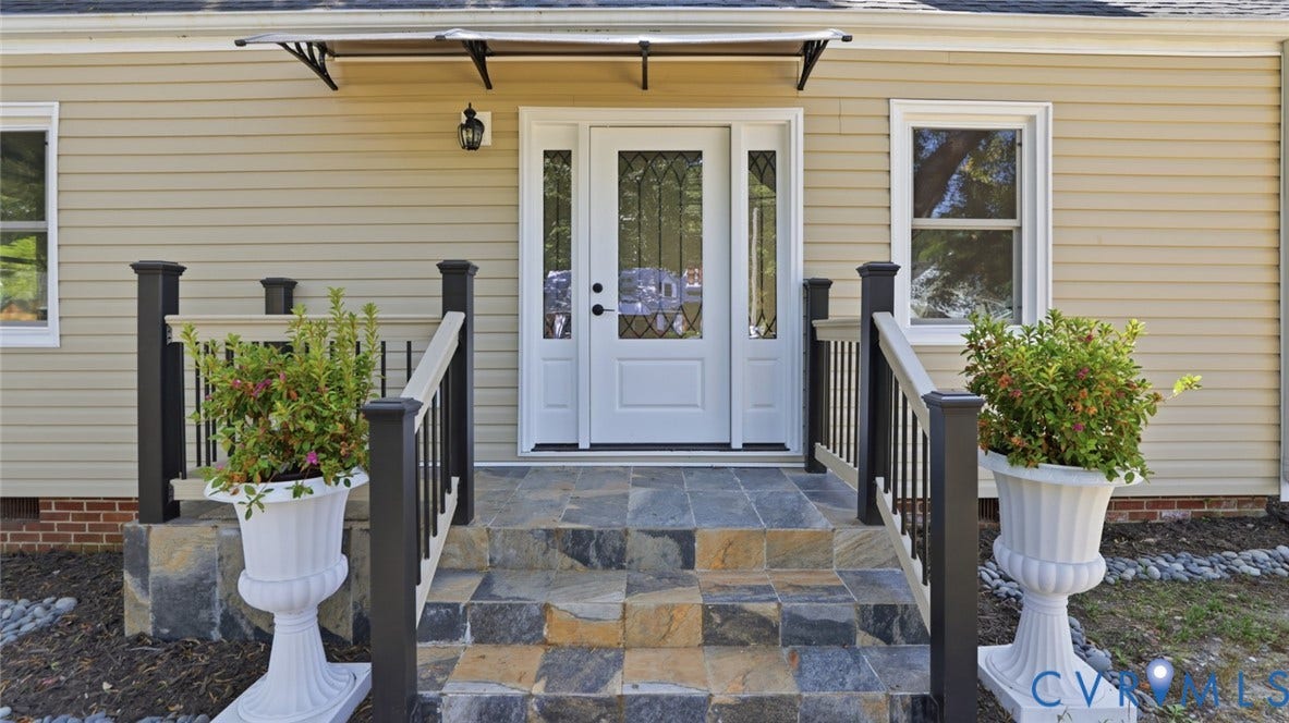 Stone veneer steps with dark-toned railings lead to a white entry door with decorative glass inserts
