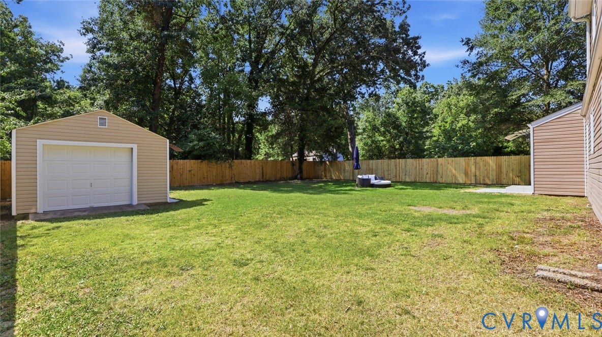 Expansive grassy yard featuring a detached garage with a white overhead door, a new wooden privacy fence, and mature perimeter trees