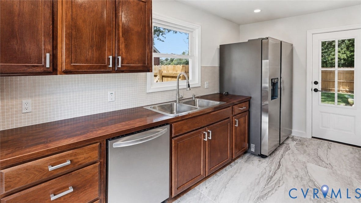 Wood cabinetry with stainless steel hardware, mosaic tile backsplash, double basin stainless steel sink, wood-finish countertops, and stainless steel appliances