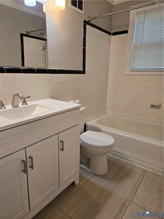 3427 W Franklin Street, Museum District, Richmond, VA 23221 Spa-inspired bathroom featuring a vanity with white cabinetry and brushed nickel hardware, ceramic tile walls with black accent trim, wood-finish flooring, and a tub-shower combination with chrome fixtures