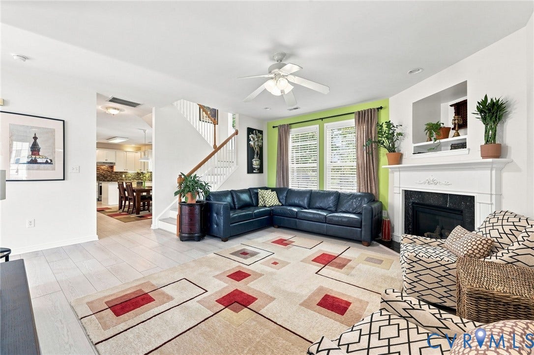 Living area featuring wood-finish flooring, a white mantel fireplace with a dark surround, and a ceiling fan