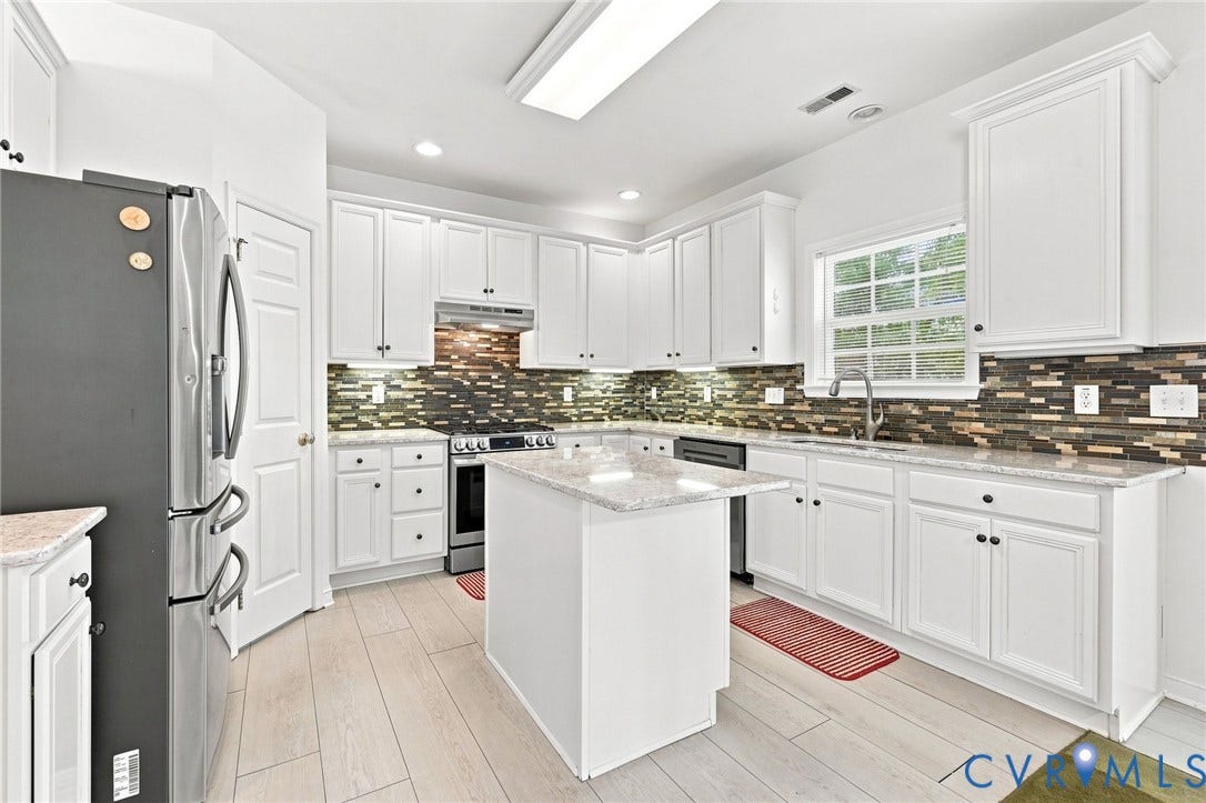 Kitchen featuring white cabinetry, light-toned wood-finish flooring, a central island with a light countertop, stainless steel appliances, and a mosaic tile backsplash