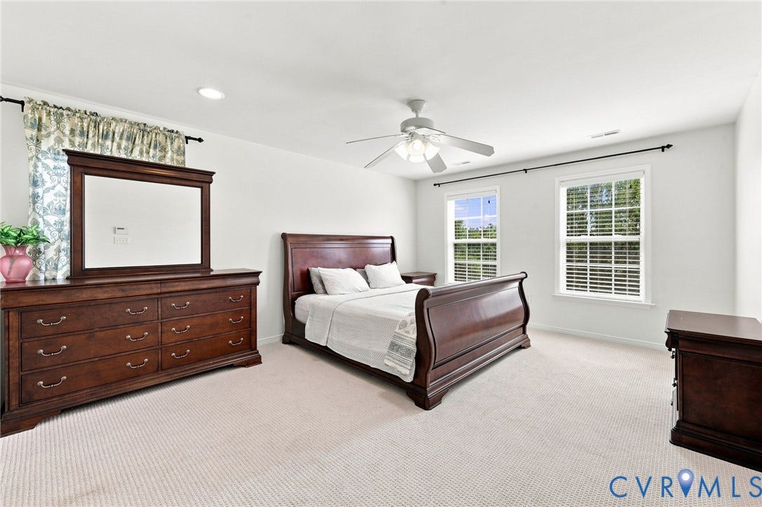 Spacious primary bedroom with elegant wood-finish furnishings, neutral carpeting throughout, and abundant natural light from multiple windows