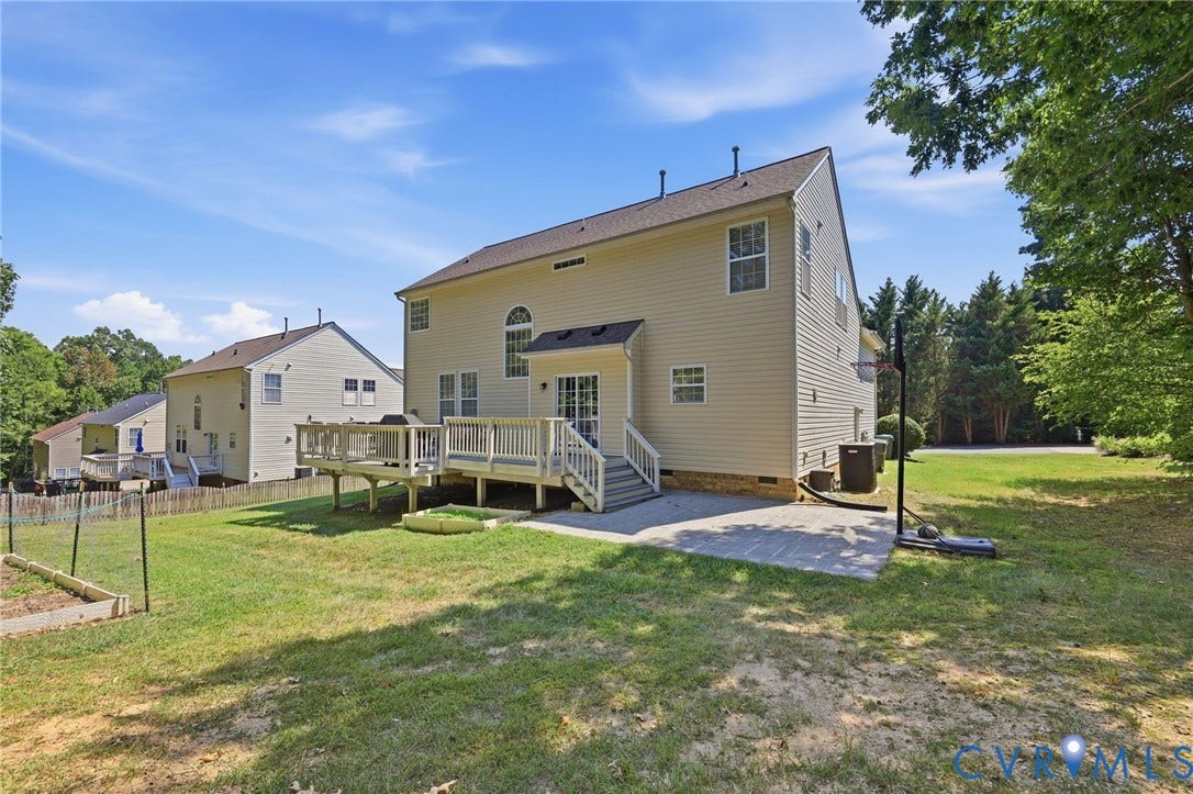 Expansive backyard featuring a wood deck, sliding glass door access, and a paved patio area