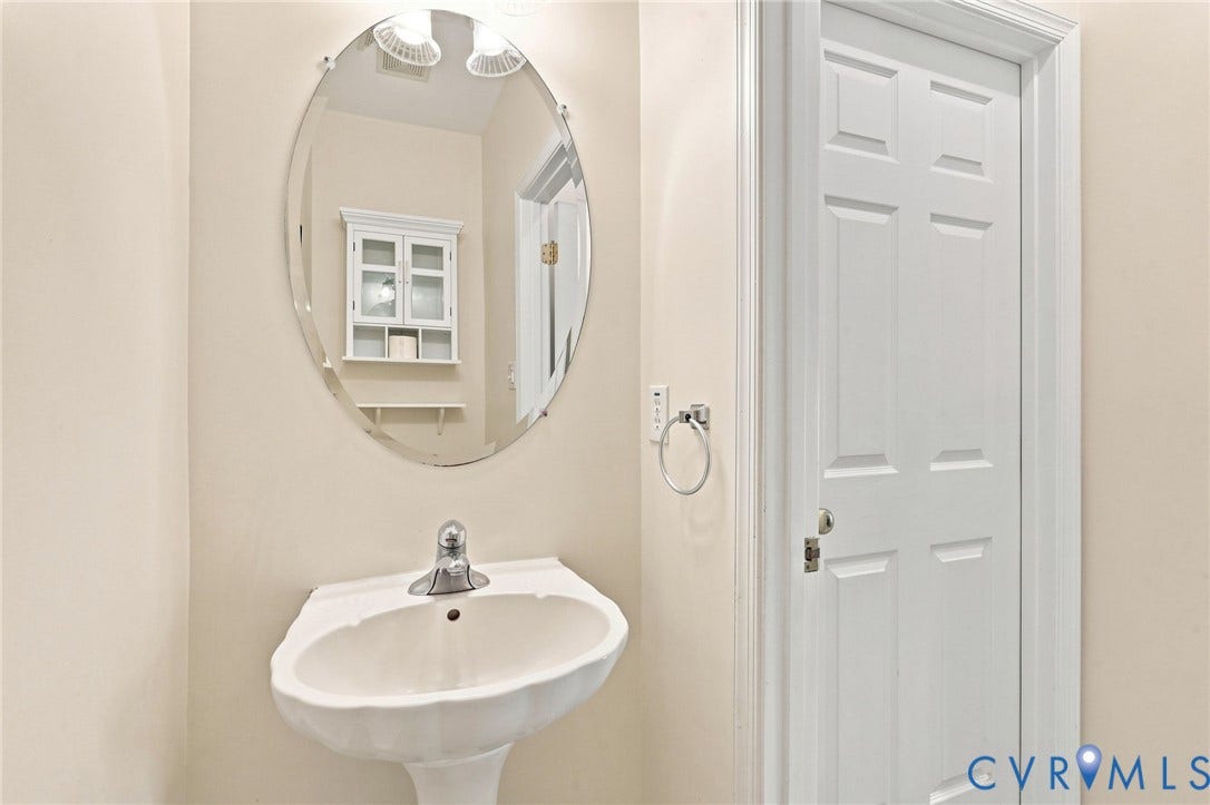 Pedestal sink with chrome faucet, oval wall mirror, and overhead vanity lighting