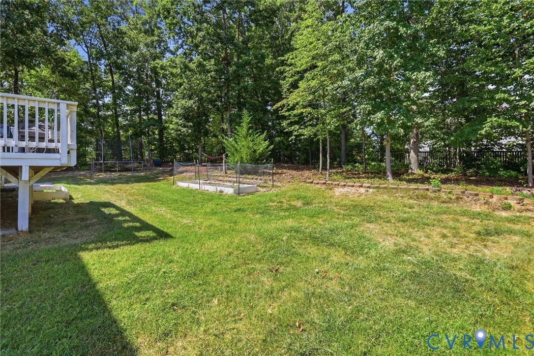 Expansive green lawn with mature trees, raised garden beds, and a white wood deck