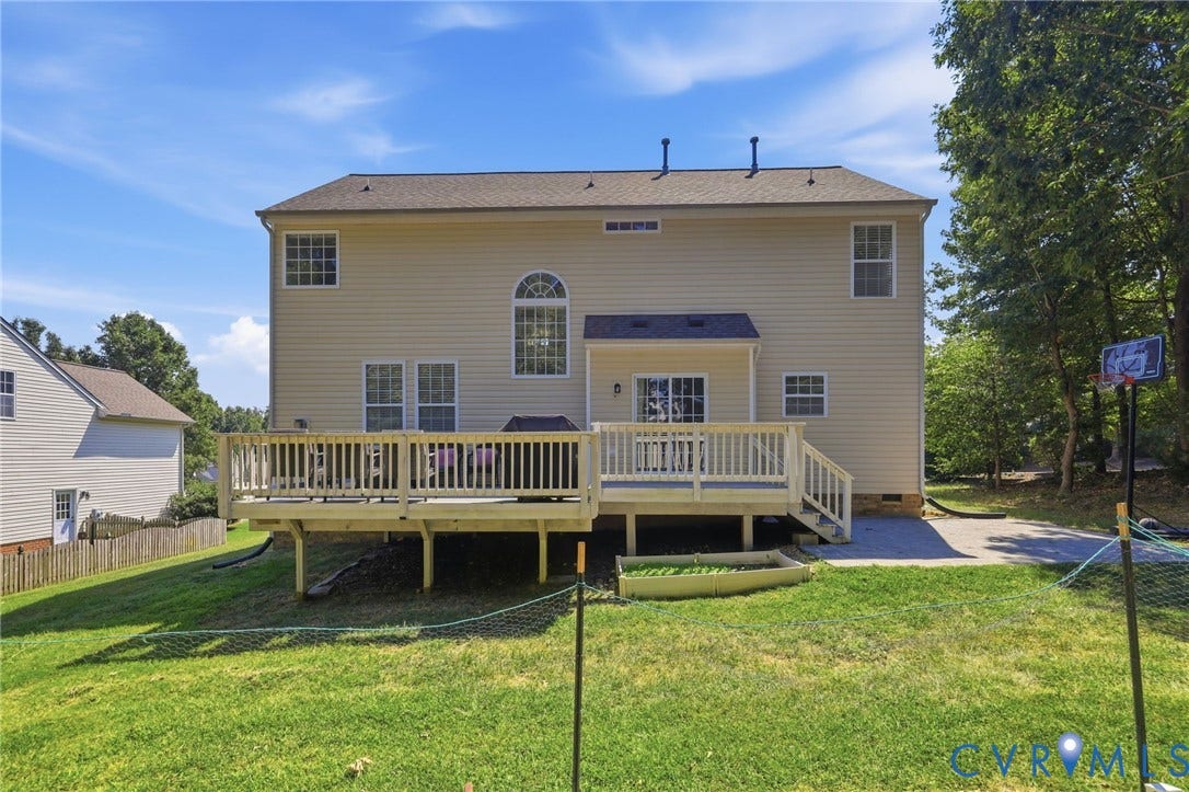 Rear exterior featuring a spacious wooden deck, sliding glass doors, multiple windows, and a paved patio area