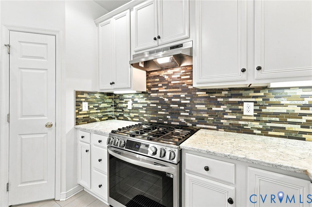 White cabinetry with black hardware, mosaic tile backsplash, stainless steel range and hood, and light-toned countertops