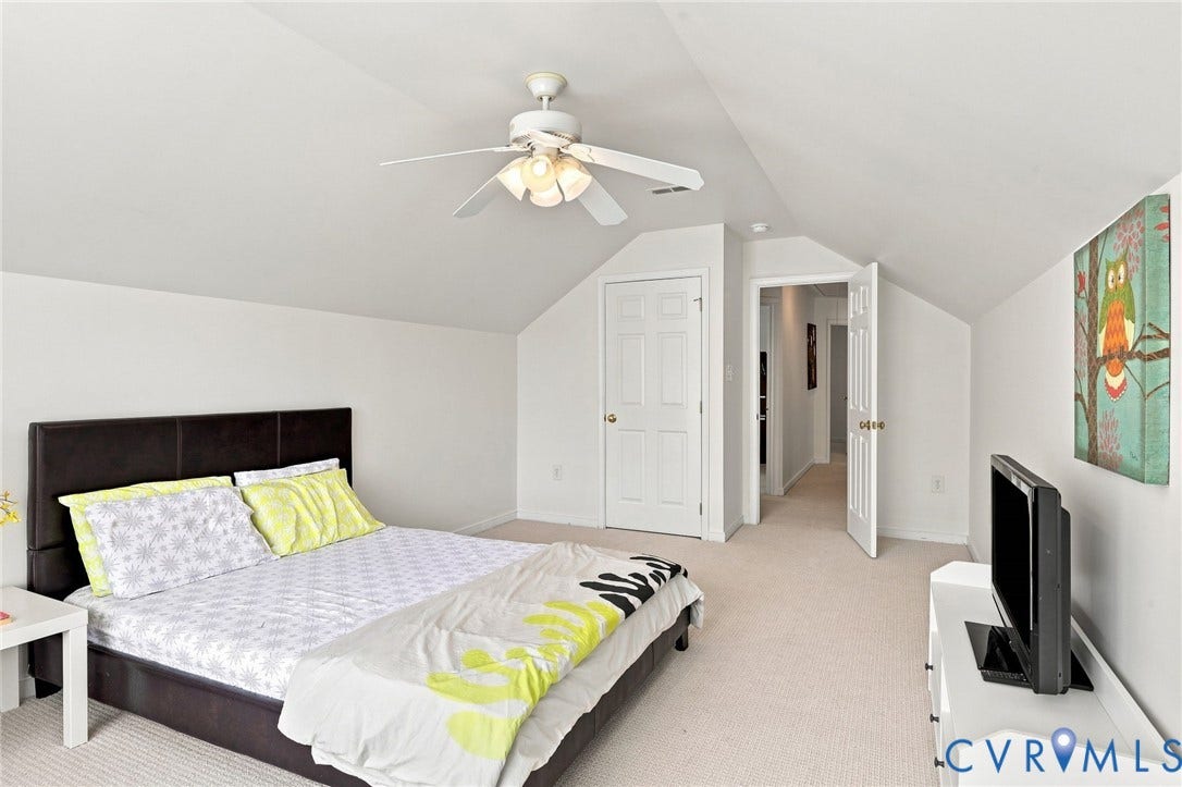 White walls with a sloped ceiling, overhead ceiling fan, and light-toned carpeting