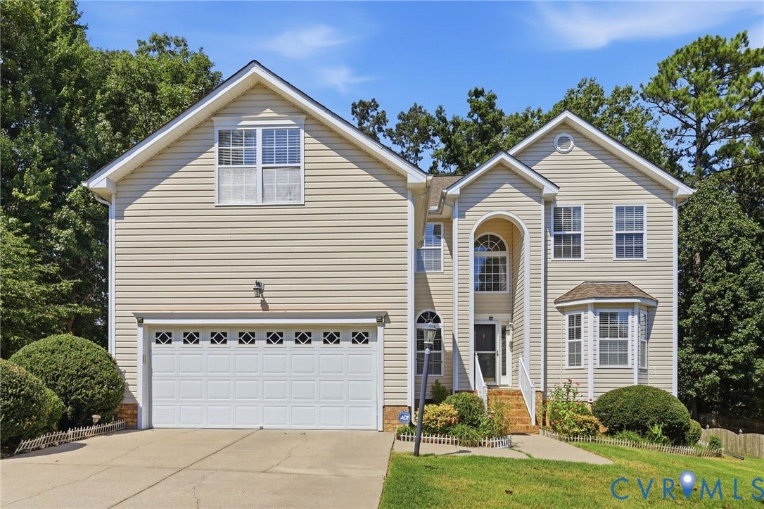 Traditional two-story residence with a two-car garage, bay window, arched entryway, and mature landscaping