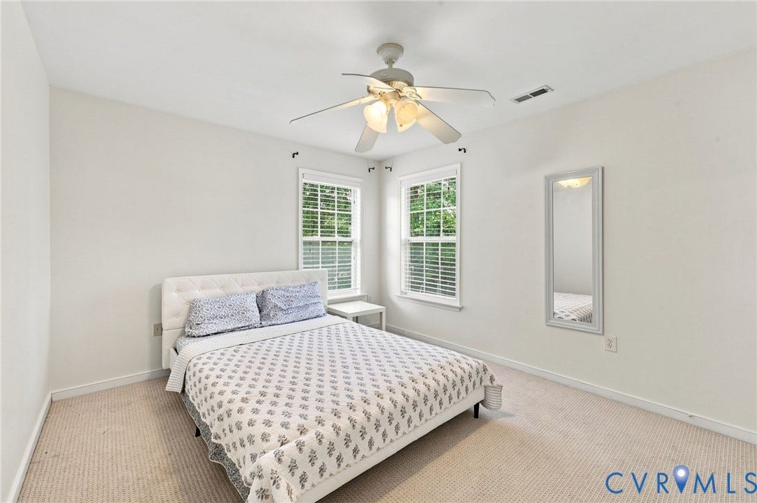 Plush carpet flooring, ceiling fan with integrated lighting, and two windows with blinds